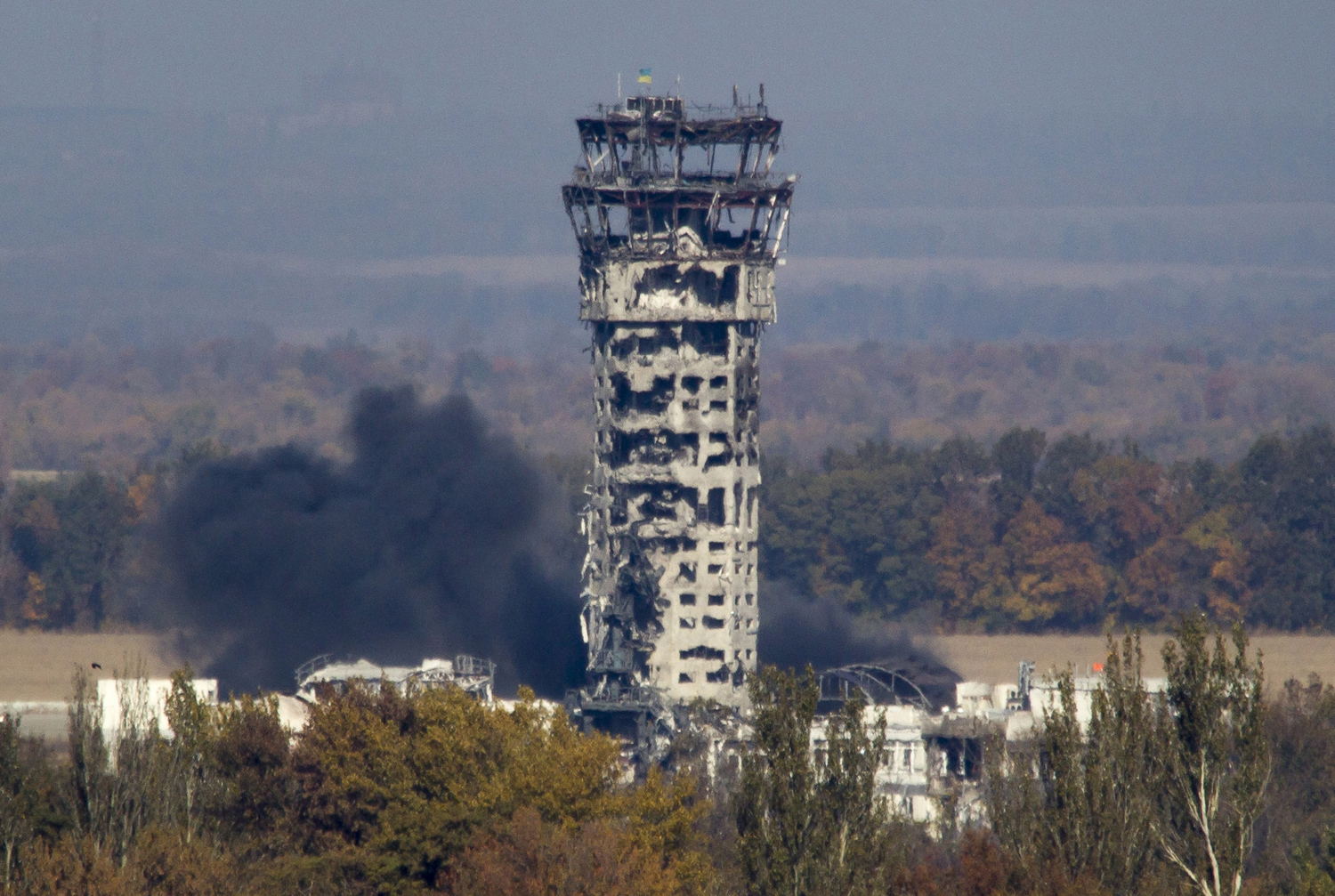A Ukrainian national flag flies at top of a badly damaged traffic control tower as smoke rises after shelling at the airport on October 12, 2014.