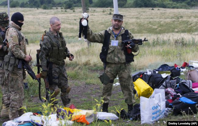 Боевик российских гибридных сил держит игрушку, обнаруженную на месте падения обломков «Боинга», сбитого российской установкой «Бук», в результате чего погибли 298 человек, в том числе 80 детей. Донецкая область, близ села Грабово, 19 июля 2014 года