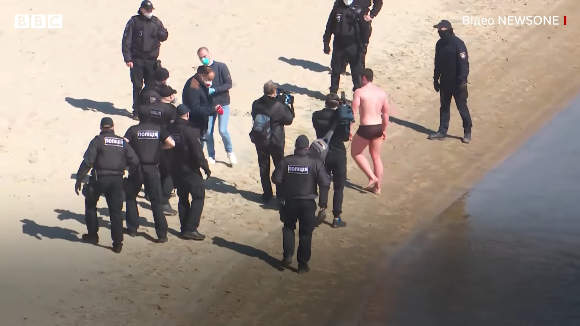 Police detain a man who protesting against the quarantine-related ban on visiting sports grounds has swum across the Dnipro River in Kyiv heading towards a popular open-air gym on a river island. Kyiv, 6 April 2019. A day later, reports emerged on coronavirus deaths of two men in Kyiv at the ages of 30 and 35. Screenshot: NewsOne via BBC Ukraine.