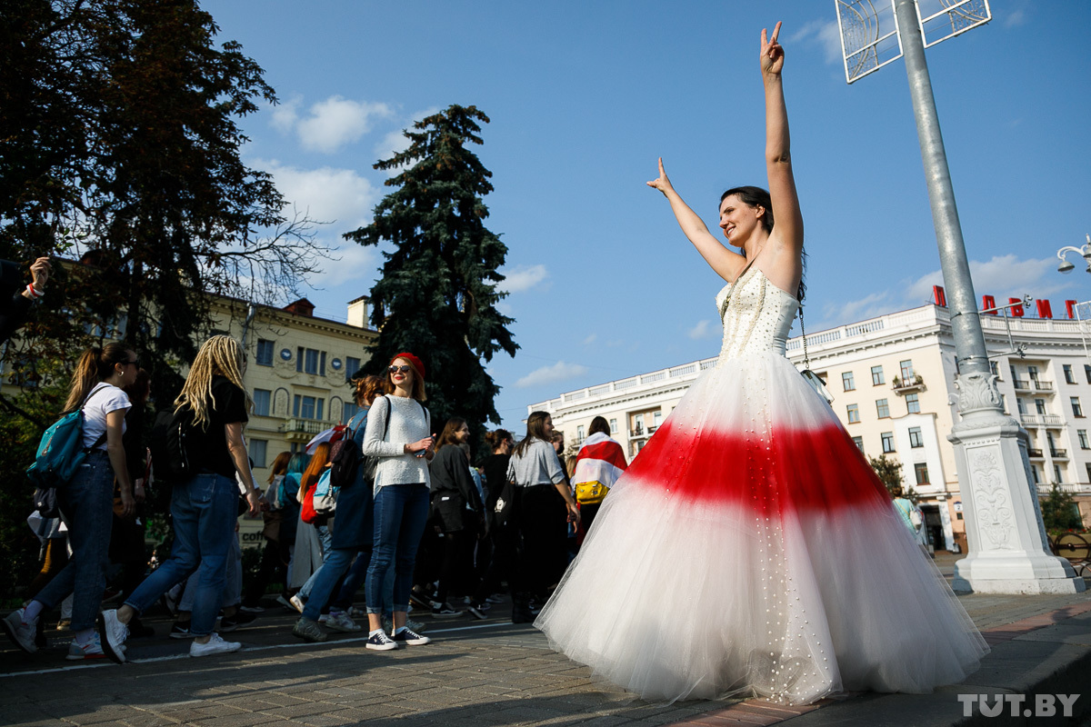 A woman in a wedding dress painted in the colors of the Belarusian “opposition” national flag greets participants of the Women’s March. Photo: Olga Shukailo, tut.by ~