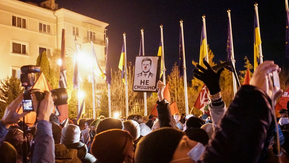 Protesters near President’s office. The caption for Zelenskyy’s portrait reads, “Not funny” implying his comedic past. Kyiv, 1 December 2021. Photo: Suspilne ~