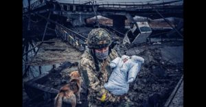 Ukrainian defender carries a baby over a river using the remains of a bridge destroyed by Russian bombardment in an area of continued Russian attacks. March 4, 2022. The Russo-Ukrainian War (2014-present). Credit: Ukrainian Freedom