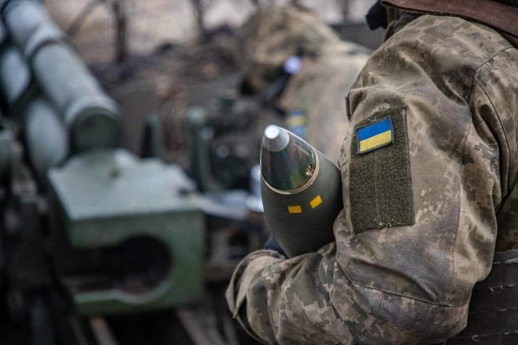 Ukrainian soldiers carry an artillery shell.