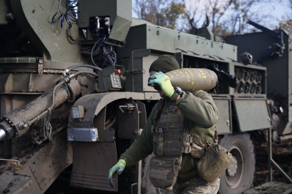 Ukrainian soldiers carry an artillery shell.