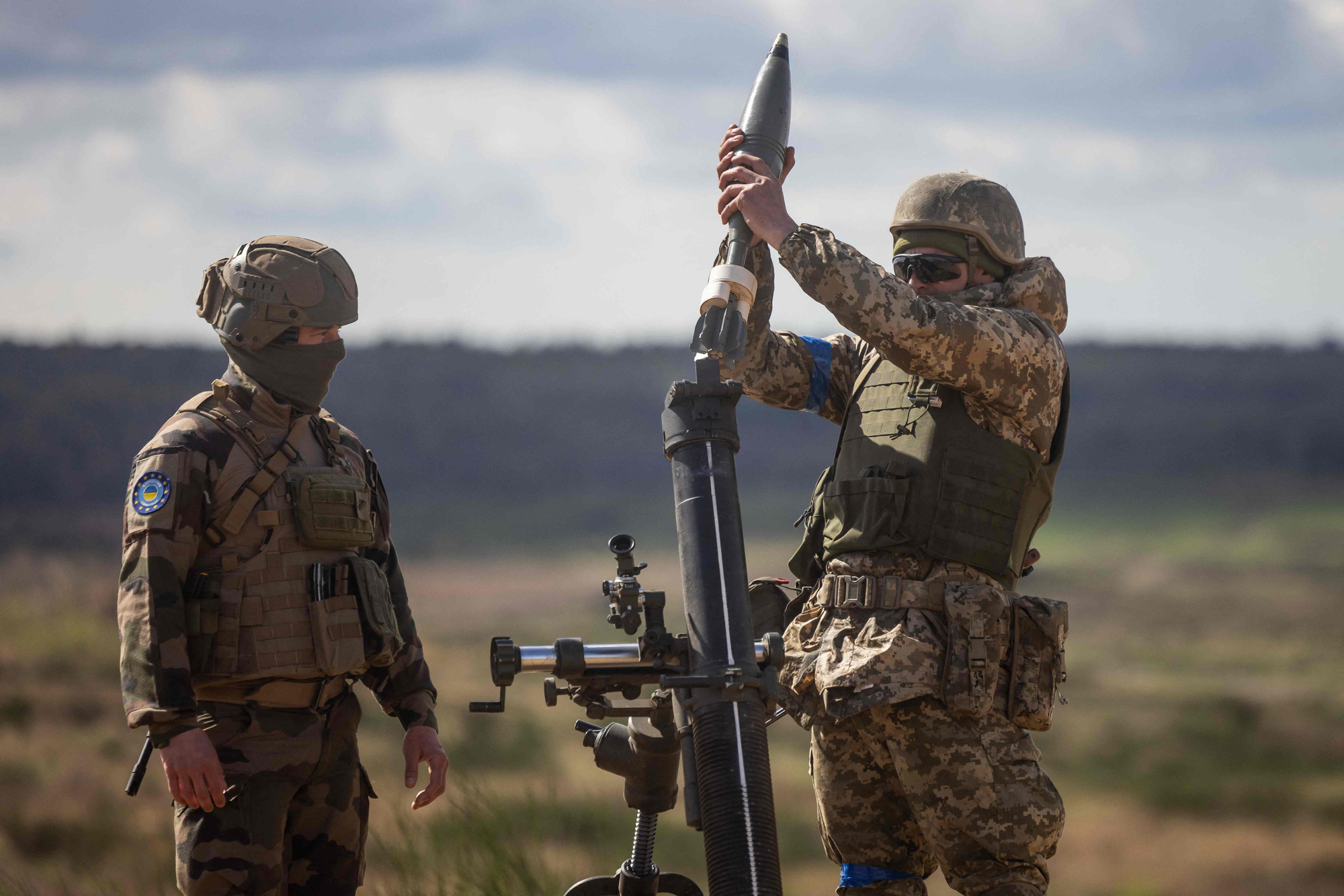 A Ukrainian soldier loads a mortar shell under the supervision of a French army instructor (L) during a military training with French servicemen, in a military training compound at an undisclosed location in Poland