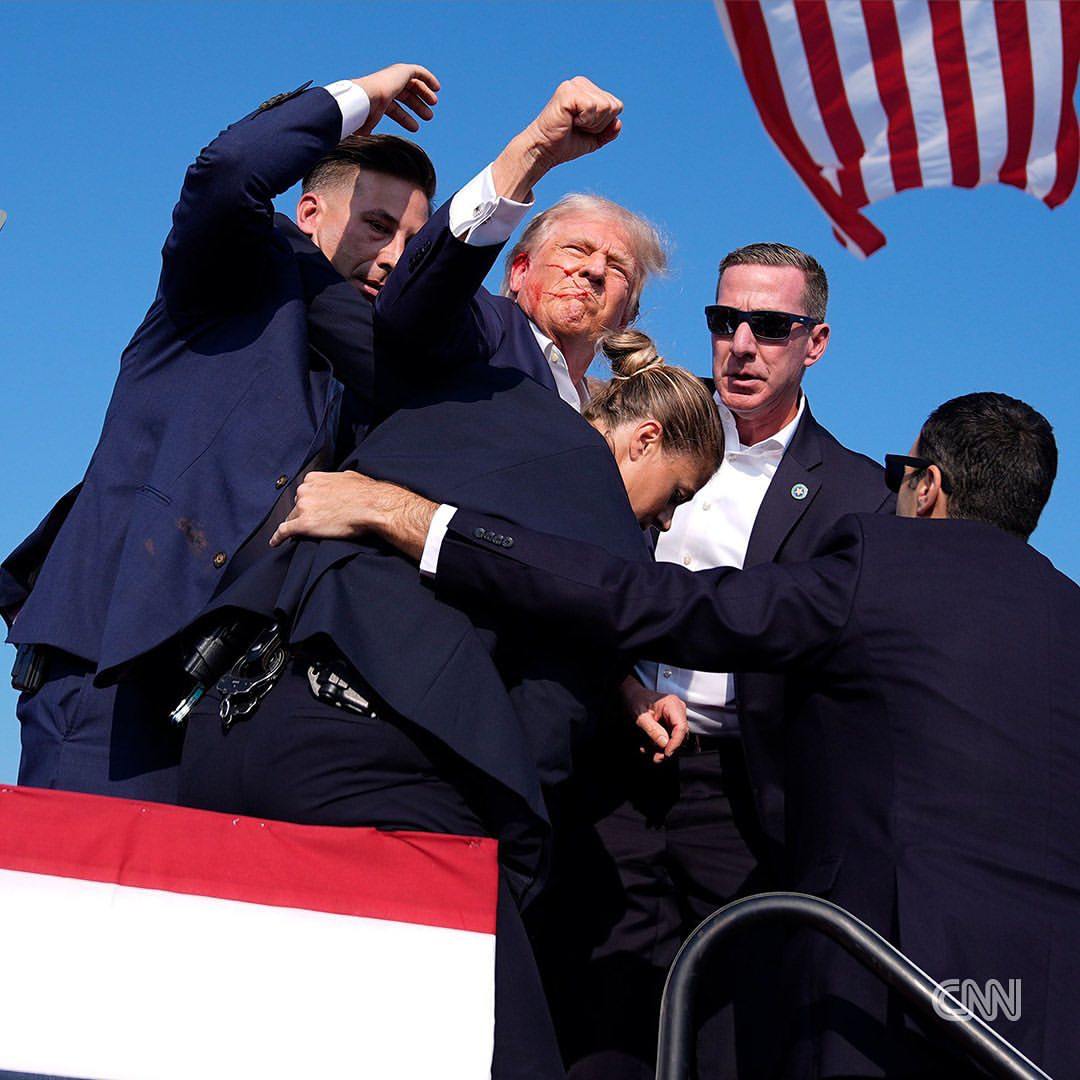 Former President Donald Trump, with blood on his face, raises his fist to the crowd as he is surrounded by Secret Service agents at his campaign rally in Butler, Pennsylvania.