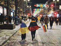 Two people walking the street in Lithuania and wearing Ukrainian (left) and Lithuanian (right) flags.