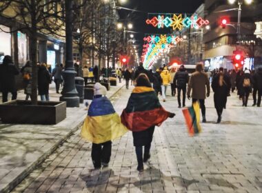 Two people walking the street in Lithuania and wearing Ukrainian (left) and Lithuanian (right) flags.