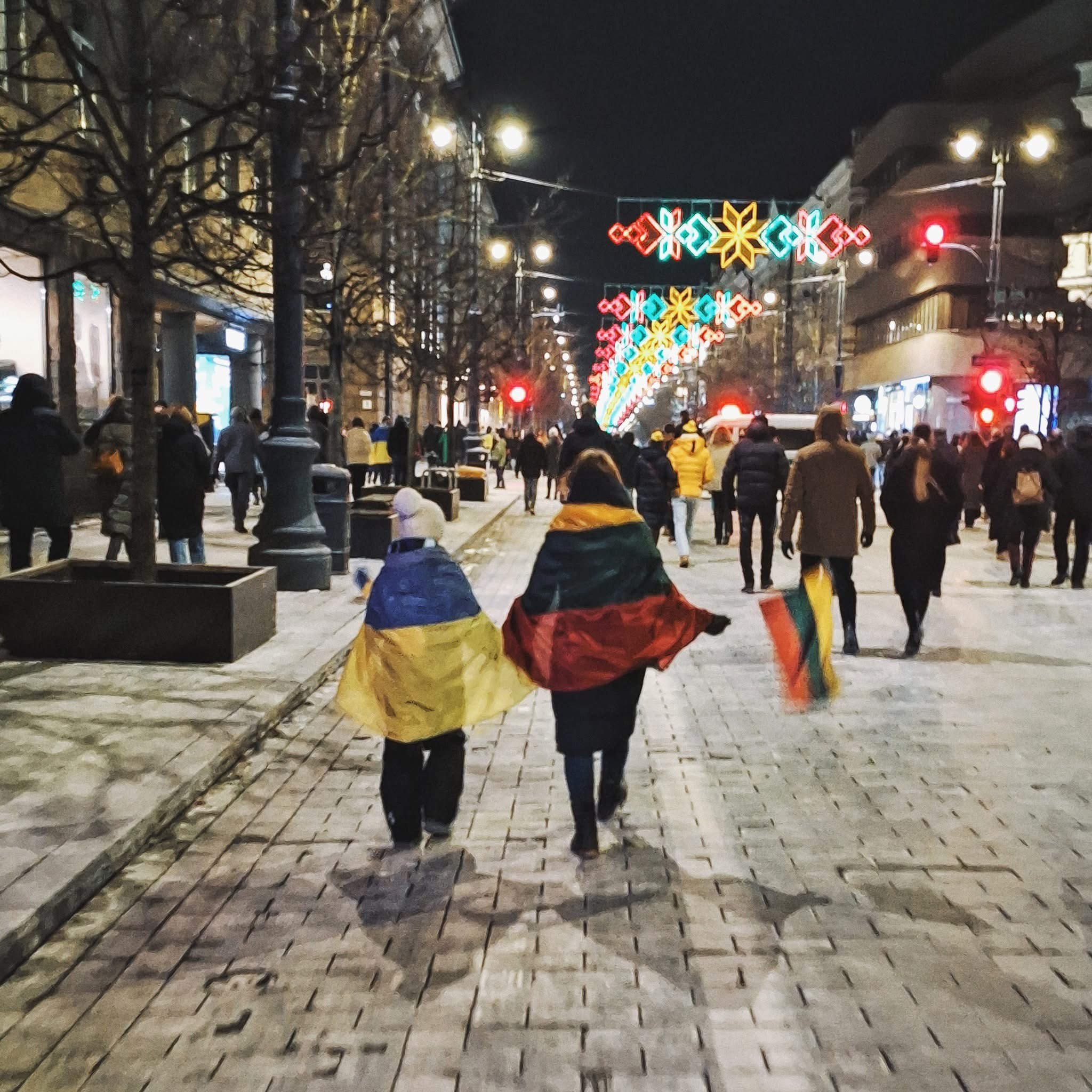 Two people walking the street in Lithuania and wearing Ukrainian (left) and Lithuanian (right) flags.