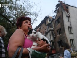 russia strikes kyiv 10 hours—two women killed including 22-year-old metro police officer woman holds cat front residential building damaged russian shahed drone 2025 people watch burn after attack suspilne news