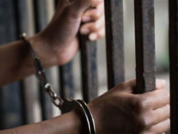 Handcuffed hands holding prison bars.
