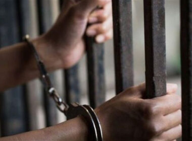 Handcuffed hands holding prison bars.