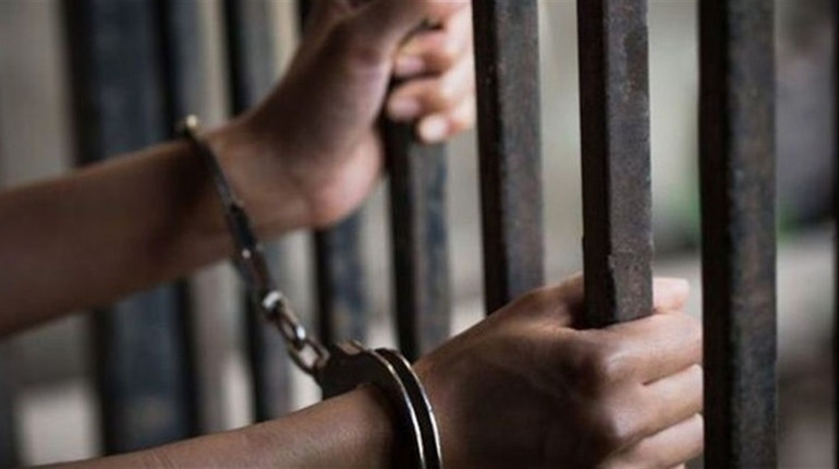 Handcuffed hands holding prison bars.