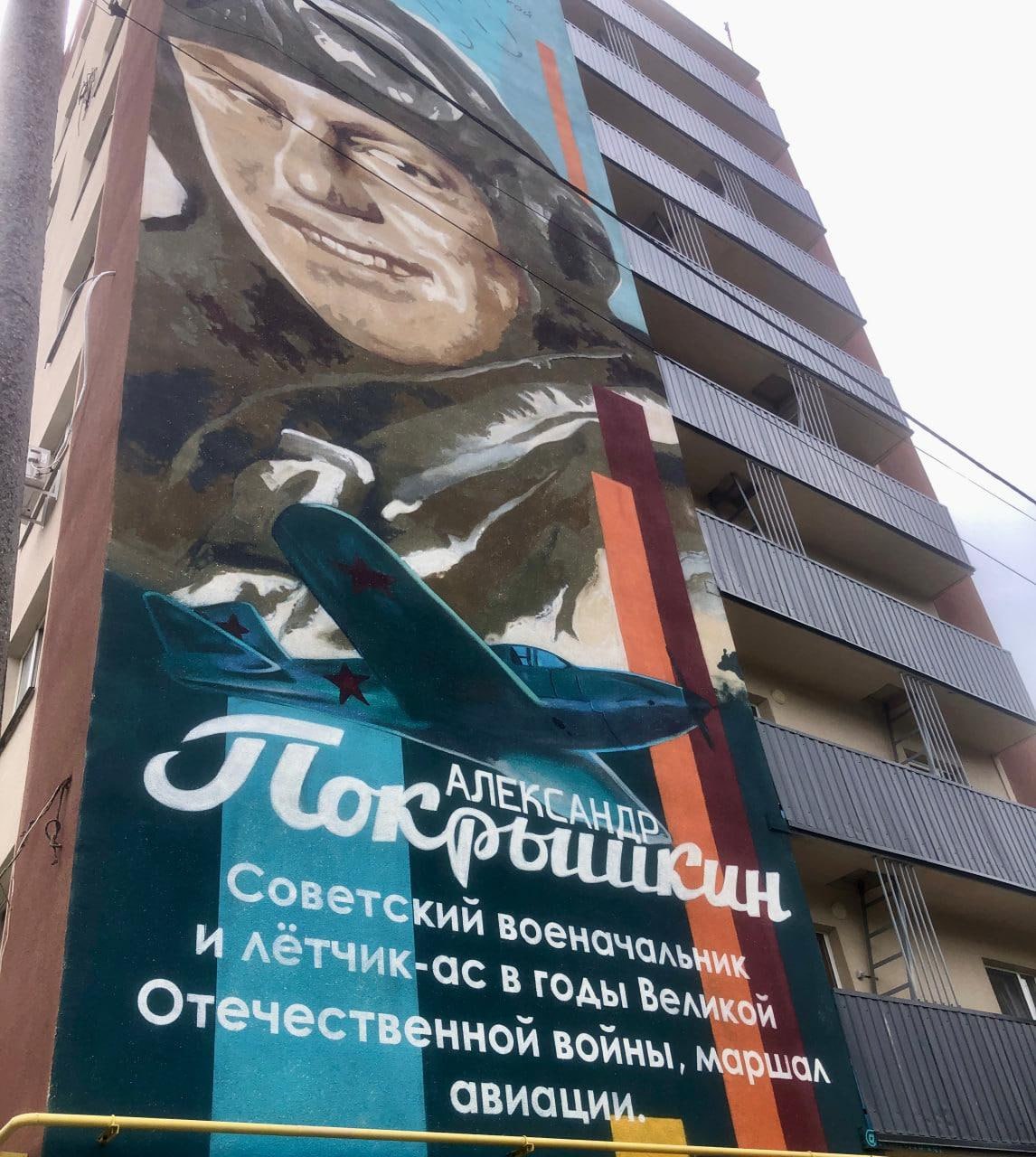 The Russian text reads: "Alexander Pokryshkin - Soviet military commander and pilot-ace during the Great Patriotic War, marshal of aviation." This mural exemplifies the systematic replacement of Ukrainian cultural symbols with Russian military glorification that occupation authorities have implemented throughout Mariupol.