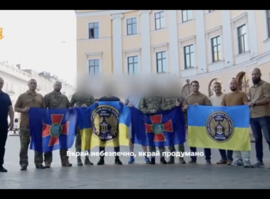 Four Ukrainian soldiers hold National Guard and naval flags following their evacuation by special forces from a hospital on Russian-occupied territory where they had been hiding since 2022. Their faces are blurred for security reasons.