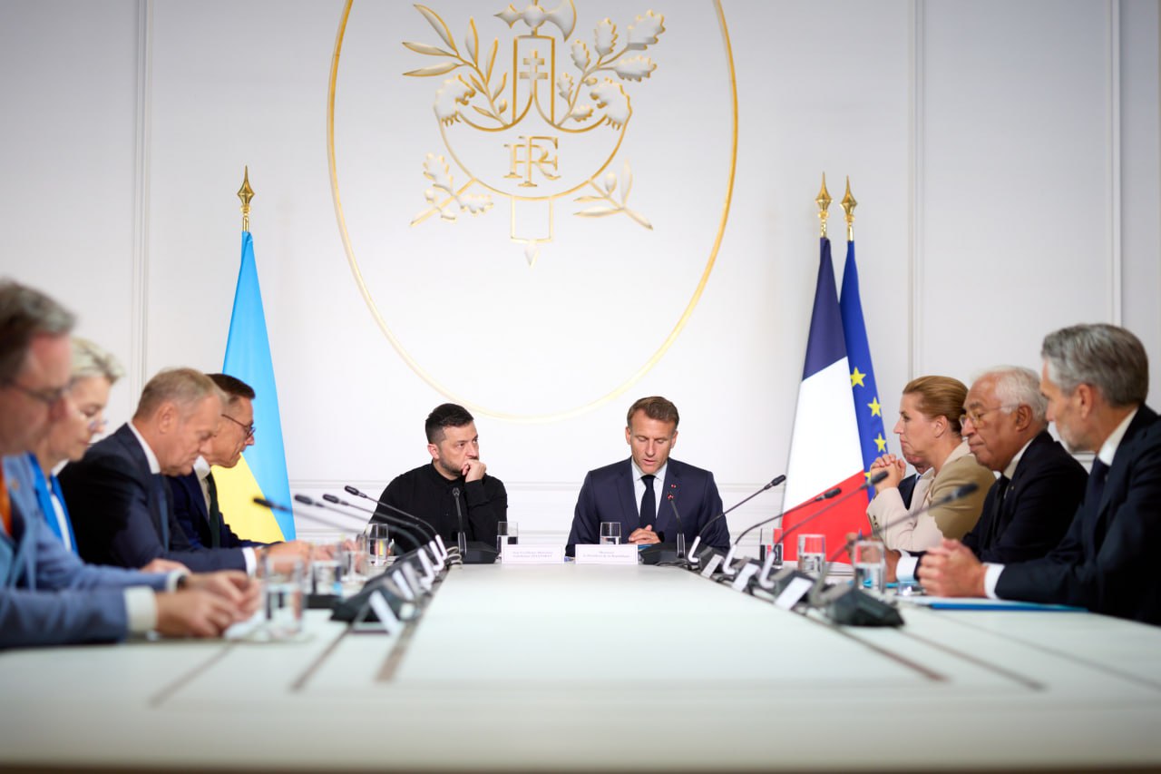 Ukrainian President Volodymyr Zelenskyy sits at a conference table with French President Emmanuel Macron and other European leaders during a Coalition of the Willing meeting.