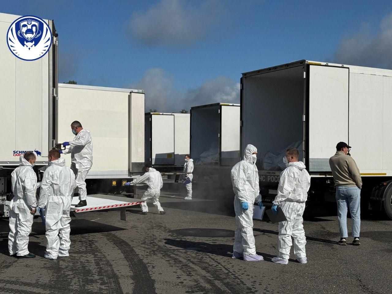 Trucks loaded with bodies of Ukrainian soldiers, accompanied by people in protective gear.