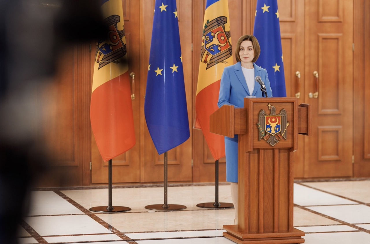 Moldovan President Maia Sandu stands at a podium, positioned between the flag of Moldova and the flag of the European Union