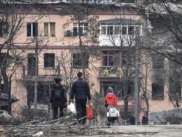 Ukrainian displaced family walks past a war-damaged apartment building in an occupied area