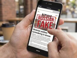 Hand holding smartphone displaying fake news article about Ukrainian soldiers surrendering, stamped with "Russian Fake" label