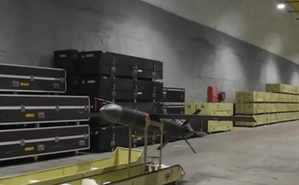 Iranian Shahed-107 attack drone on a trolley inside a storage facility, with stacks of black and yellow ammunition or equipment crates in the background