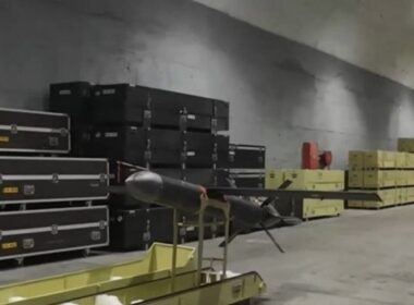 Iranian Shahed-107 attack drone on a trolley inside a storage facility, with stacks of black and yellow ammunition or equipment crates in the background