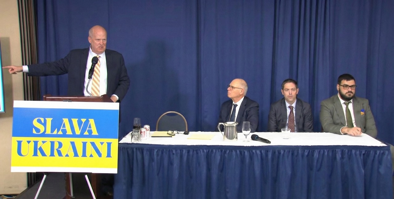 Attorney Mikal Watts speaks at podium with "Slava Ukraini" sign, announcing lawsuits against Intel, AMD, and Texas Instruments over chips found in Russian missiles, National Press Club, Washington D.C.
