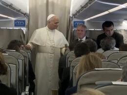 Pope Leo XIV in white papal vestments addresses journalists in the cabin of an ITA Airways plane during an inflight press conference returning from Turkey and Lebanon