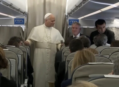 Pope Leo XIV in white papal vestments addresses journalists in the cabin of an ITA Airways plane during an inflight press conference returning from Turkey and Lebanon