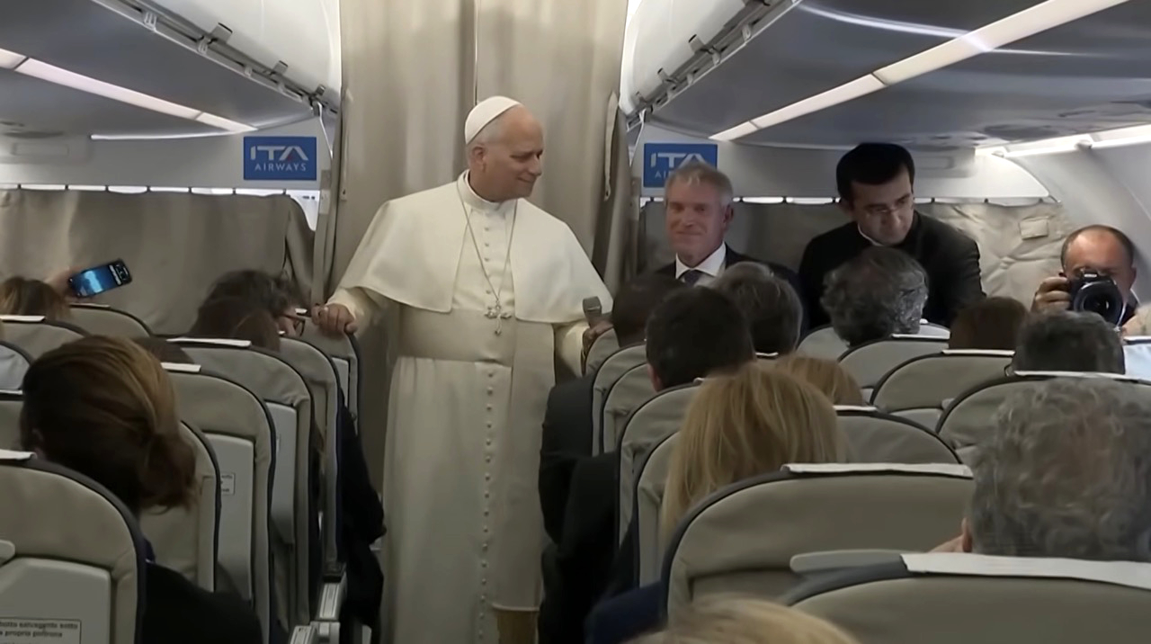 Pope Leo XIV in white papal vestments addresses journalists in the cabin of an ITA Airways plane during an inflight press conference returning from Turkey and Lebanon