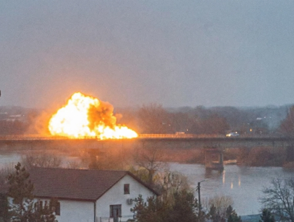 Explosion and fireball on a bridge over the Dniester river, with a residential house in the foreground and gray winter sky