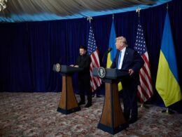 Volodymyr Zelenskyy and Donald Trump stand at podiums during a joint press conference at Mar-a-Lago, with US and Ukrainian flags behind them
