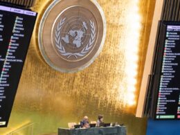 Electronic voting boards display country-by-country votes during a UN General Assembly session on Ukraine, with the UN emblem visible in the center of the hall