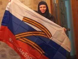 A nun from the St. Elizabeth Monastery in Sweden holds a Russian flag bearing the "Z" war symbol and St. George ribbons. Photo via The Telegraph