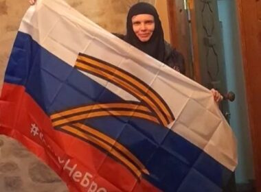A nun from the St. Elizabeth Monastery in Sweden holds a Russian flag bearing the "Z" war symbol and St. George ribbons. Photo via The Telegraph