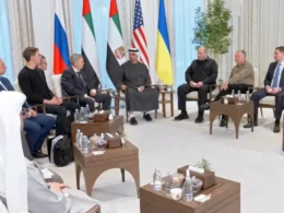 Delegations from Russia, the United States, and Ukraine sit in a formal meeting room in Abu Dhabi with UAE President Mohamed bin Zayed Al Nahyan at center, flanked by Russian, UAE, US, and Ukrainian flags.