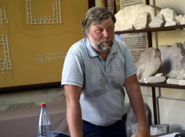 Alexander Butyagin, Russian archaeologist from the Hermitage Museum, standing in front of archaeological artifacts and a site map in occupied Crimea