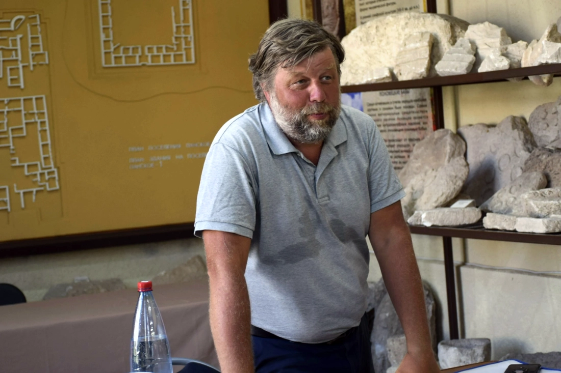 Alexander Butyagin, Russian archaeologist from the Hermitage Museum, standing in front of archaeological artifacts and a site map in occupied Crimea