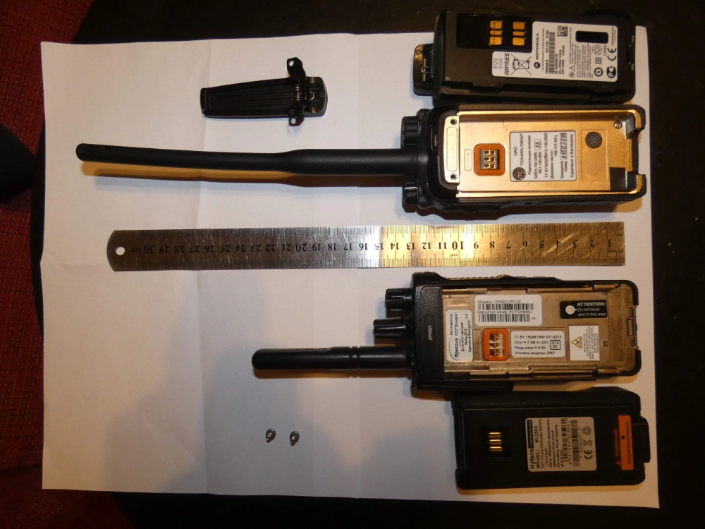 Two professional military-grade handheld radios with batteries and antennas laid out on paper with a ruler for scale