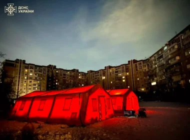 Orange State Emergency Service heated tents illuminated at night in front of Kyiv apartment buildings, some windows lit while others remain dark during blackouts