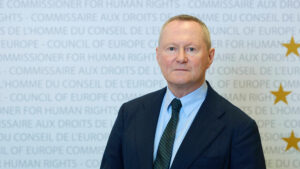 Michael O'Flaherty, Council of Europe Commissioner for Human Rights, standing in front of a blue backdrop with Council of Europe branding and gold stars