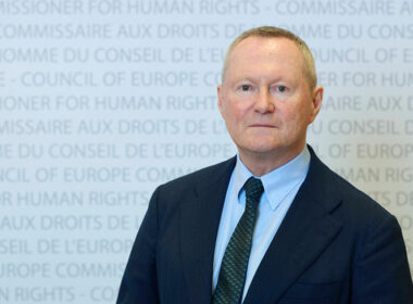Michael O'Flaherty, Council of Europe Commissioner for Human Rights, standing in front of a blue backdrop with Council of Europe branding and gold stars