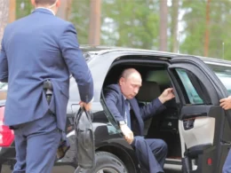 Russian President Vladimir Putin exits a black limousine while security personnel in blue suits attend to him