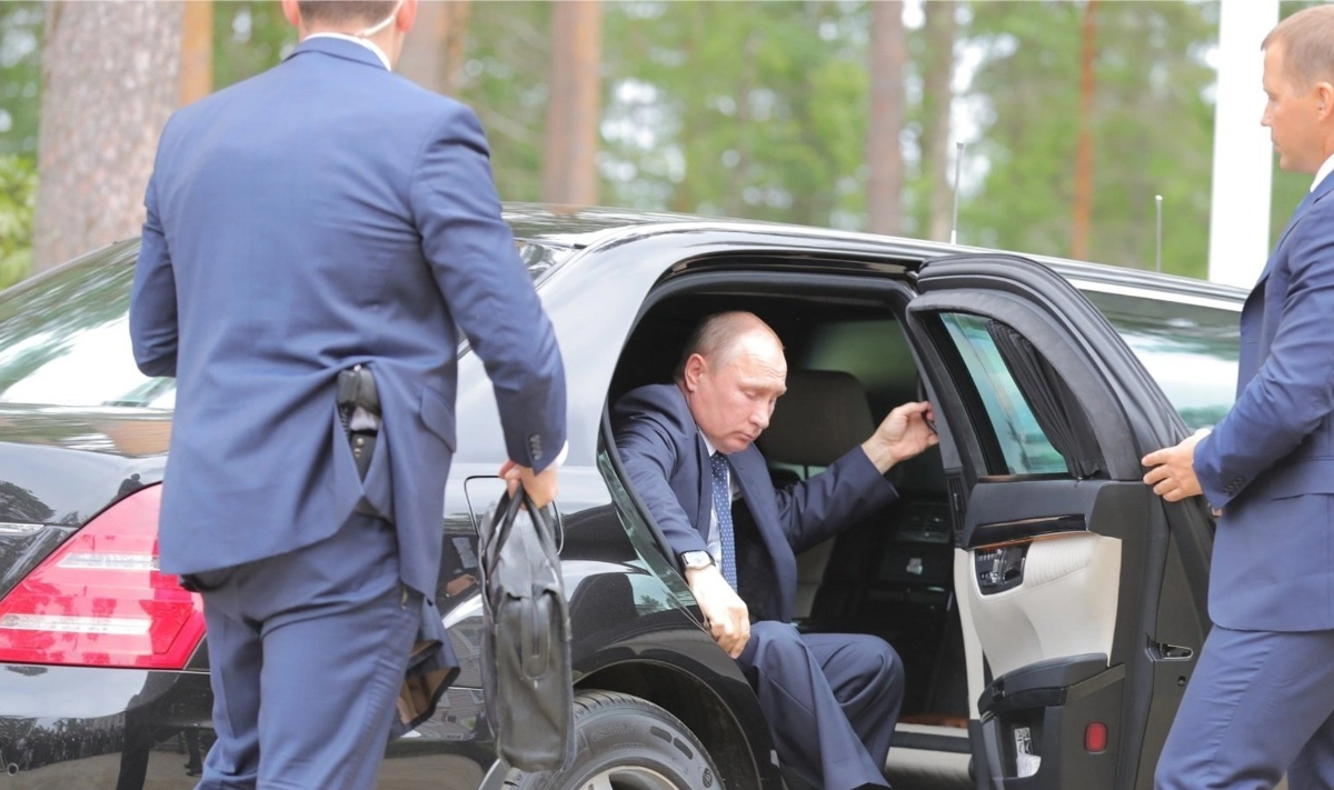 Russian President Vladimir Putin exits a black limousine while security personnel in blue suits attend to him