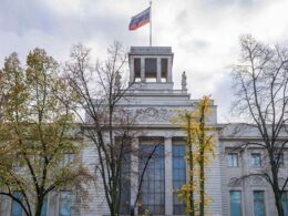 The Russian Embassy building in Berlin with the Russian flag flying on top, partially obscured by autumn trees