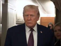 President Donald Trump in a navy suit and red tie aboard Air Force One, speaking to reporters about Iran on 11 January 2026