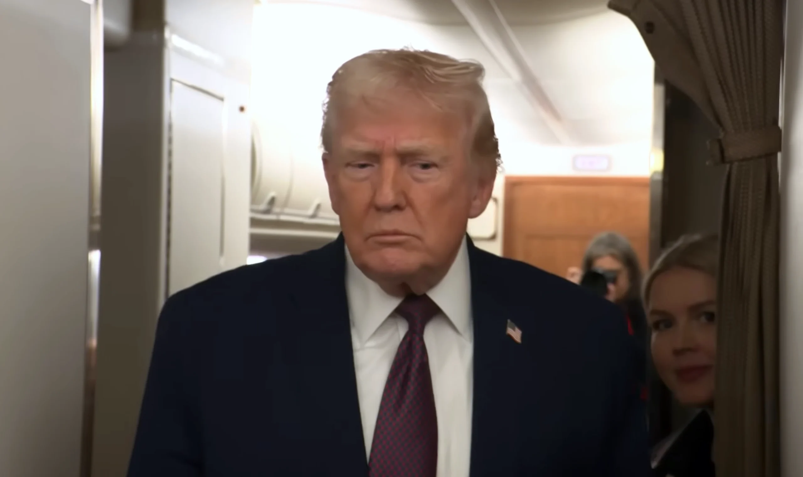 President Donald Trump in a navy suit and red tie aboard Air Force One, speaking to reporters about Iran on 11 January 2026