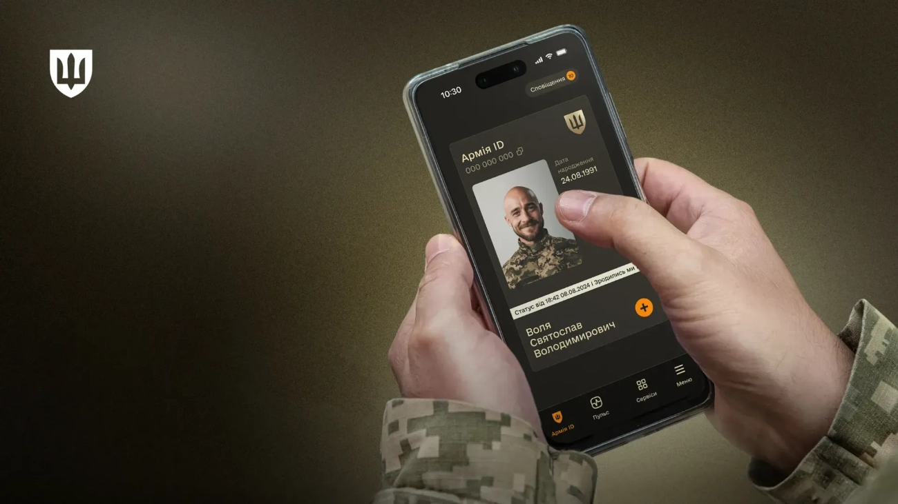 Ukrainian soldier in pixelated camouflage holds smartphone showing Army+ app with digital military ID displaying photo, name, and birth date