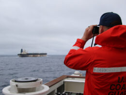US Coast Guard crew member in orange jacket looks through binoculars at the oil tanker Marinera from aboard the cutter Munro in the North Atlantic