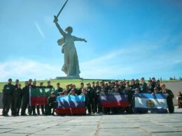 Ukrainian teenagers in Avangard camp uniforms pose with flags of four Russian-occupied Ukrainian regions in front of the Motherland Calls statue at Mamayev Kurgan in Volgograd